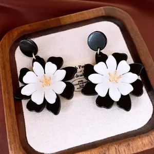 Détail rapproché d'élégantes boucles d'oreilles fleurs en acrylique noir et blanc avec pistil doré.