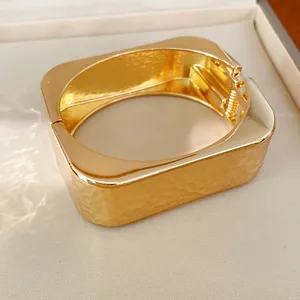 Primer plano detallado de un brazalete rectangular dorado de textura martillada.