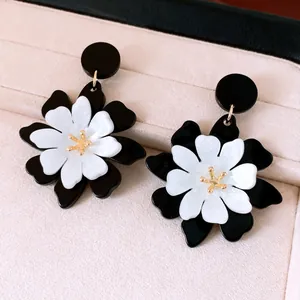 Gros plan de boucles d'oreilles fleurs en acrylique noir et blanc sur un écrin rose élégant