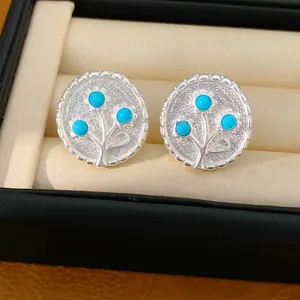 Close-up van zilverkleurige ronde oorknopjes met een fijn ontwerp van blauwe harsbloemen