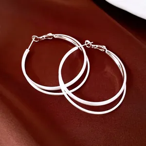 Élégantes boucles d'oreilles créoles doubles en argent sur un fond de soie foncée.
