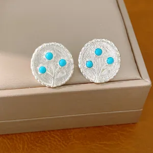 Close-up van zilveren ronde oorknopjes met blauw harsbloemontwerp.