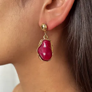 Close-up of vintage gold earring with an irregular red resin stone drop on a model's ear