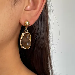Detailed close-up of retro gold metal earrings featuring an irregular brown resin dangle