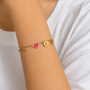 Detail van gouden armband met rood hart, roze zirkoon en letter A-bedel
