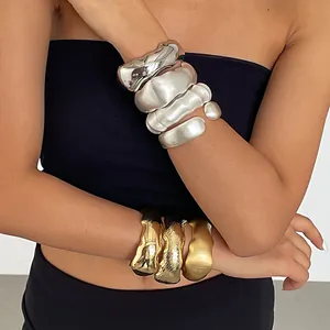 Klobige wellenförmige metallische geometrische Armreifen in Silber- und Goldtönen.