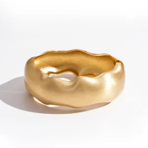 Eleganter breiter goldener Armreif mit Wellenstruktur und matter geometrischer Oberfläche.