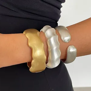 Detailaufnahme von massiven, matten Gold- und Silberwellen-Armreifen am Arm eines Models