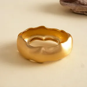 Detailansicht eines klobigen, mattgoldenen, welligen geometrischen Metallarmreifens im Retro-Stil