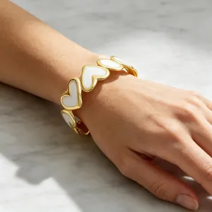 Vista detallada de un brazalete de corazón bañado en oro de 18k con esmalte blanco en la muñeca