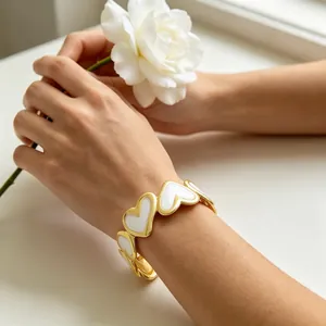 Vista detallada de un brazalete en C bañado en oro con corazones de esmalte blanco