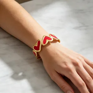 Detalle de una pulsera rígida dorada con corazones de esmalte rojo en una muñeca