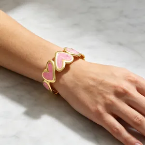 Vista detallada de un brazalete esmaltado en forma de corazón chapado en oro sobre mármol.