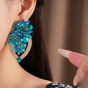 Gros plan de boucles d'oreilles pendantes fleurs en cristal bleu et vert sur une oreille.