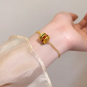 Detailed close-up of a 24K gold-plated bracelet with a red enamel charm on a woman's wrist