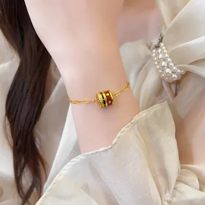 Close-up detail of 24K gold plated bracelet with red enamel cylindrical pendant on wrist