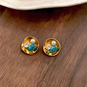 Close-up of retro gold stud earrings featuring pearl, zircon, and turquoise inlay details