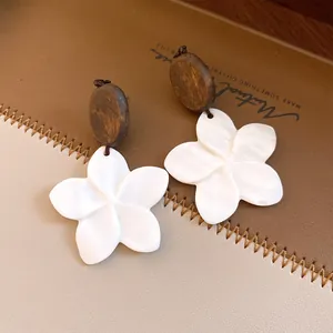 Detailopname van retro oorbellen met houten knopjes en witte schelpbloem hangers