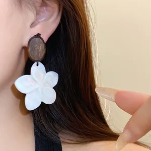 Close-up van elegante houten oorbellen met witte schelpenbloemen aan het oor.