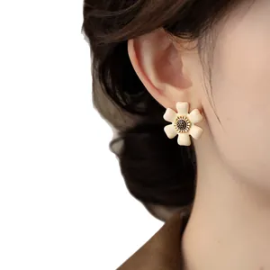 Elegant creamy white flower stud earrings with gold trim detail worn on a model's ear
