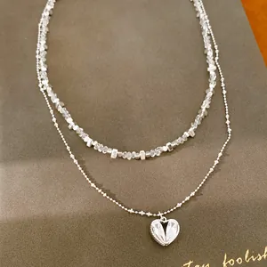 Detalle de un collar de doble capa con cuentas de vidrio y colgante de corazón de cristal.