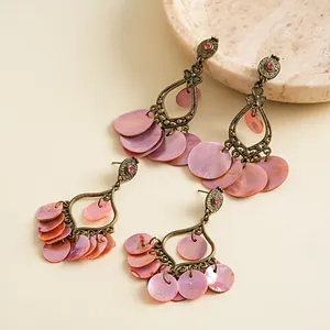 Vintage-Ohrringe aus Bronze mit rosa Muschelscheiben und kleinen Kristallen auf Steintablett.