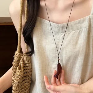 Vue détaillée d'un collier pendentif poisson en bois vintage porté sur une robe en lin.