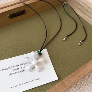 Detalle de un collar con colgante de flor geométrica en blanco mate sobre tarjeta elegante