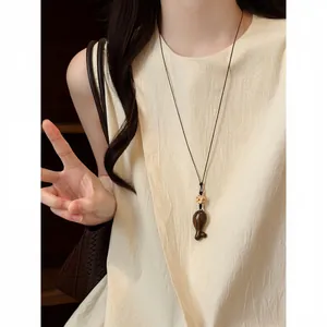 Détail d'un collier avec pendentif en bois en forme de poisson porté par un mannequin