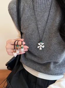Détail de pendentifs en argent brossé en forme de cœur et de trèfle sur cordon noir.