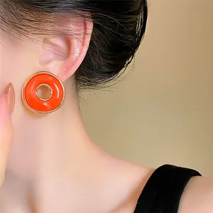 Primer plano de pendientes redondos en esmalte naranja vintage con borde de metal dorado
