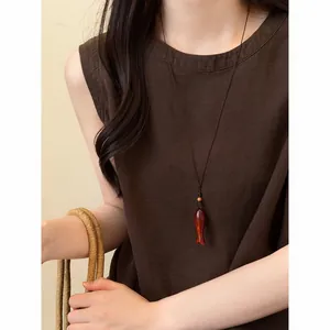 Vue détaillée d'un collier pendentif en bois en forme de poisson sur un haut en lin brun.