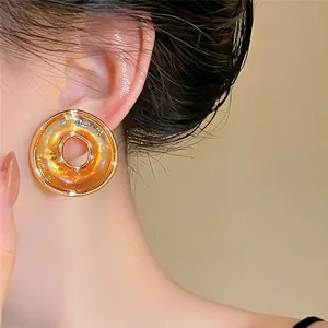 Detalle de pendientes de botón circulares dorados distorsionados en la oreja del modelo