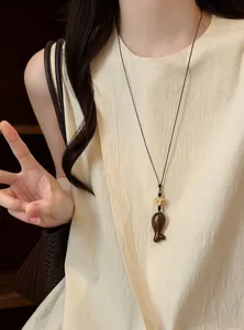 Gros plan d'un collier pendentif poisson en bois rétro porté par un mannequin élégant.