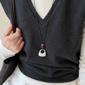 Gros plan d'un collier avec pendentif géométrique en argent brossé et perles sur un modèle.