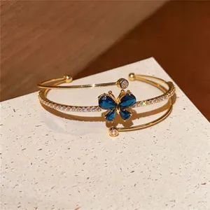 Elegante pulsera abierta multicapa dorada con mariposa de cristal azul y circonitas