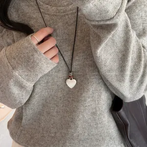Détail d'un collier avec pendentif en forme de cœur brossé argenté sur un pull gris.
