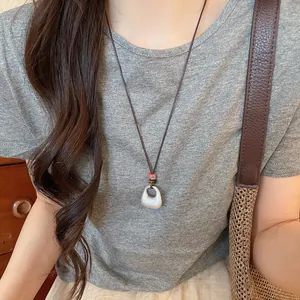 Primer plano de un collar con colgante geométrico plateado sobre camiseta gris, estilo retro