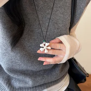 Gros plan détaillé d'un pendentif fleur blanche sur un collier de cordon noir porté par un mannequin