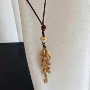Boho Muschel-Quasten-Halskette mit brauner Lederschnur und goldenen Perlen-Akzenten.