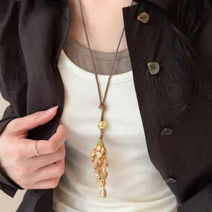 Handgefertigte böhmische Lederkordelkette mit natürlichem Muschelquastenanhänger über brauner Jacke