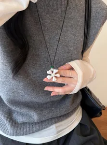 Vue détaillée d'un collier avec pendentif fleur blanche sur un débardeur gris.