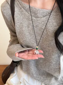 Vue détaillée d'un collier avec pendentif éléphant argenté et perles sur fond de pull gris.
