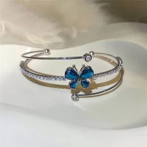 Detalle de brazalete abierto multicapa con mariposa de cristal azul y circonitas brillantes.