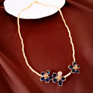 Close-up of elegant gold necklace featuring blue zircon flower pendants on brown silk.