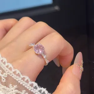 Close-up van een roze ronde zirkonia ring met zilveren bloemdetails op een hand gedragen.
