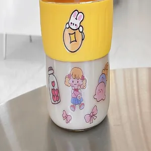 Close-up detail of cute cartoon stickers on a glass coffee cup with yellow silicone sleeve