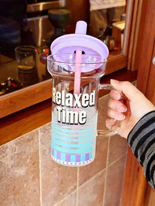 Gros plan d'une tasse en verre avec anse, couvercle violet et paille rose en main.