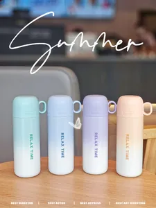 Cuatro botellas térmicas de acero inoxidable con degradado y asas en mesa de madera