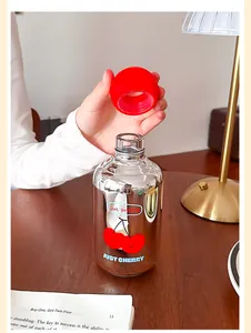 Gros plan d'une bouteille d'eau en verre miroir argenté avec motif cerise et bouchon rouge.